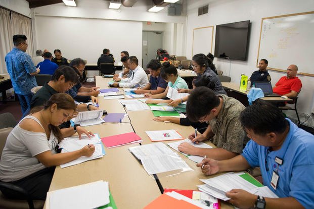 Potential applicants complete paperwork for security guard positions at a job fair held at the Federal Fire Department on Joint Base Pearl Harbor-Hickam. (U.S. Navy/Nardel Gervacio)