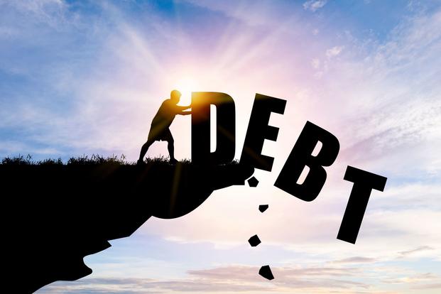 A silhouetted person pushes the letters of the word debt off a cliff