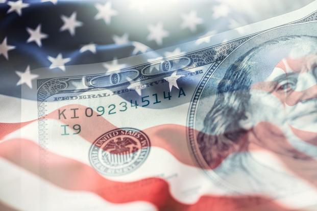 A partially transparent $100 bill is superimposed over a fluttering American flag