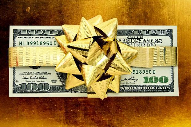 A shiny gold ribbon a bow are wrapped around a stack of $100 bills