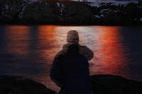 In this photo made with a long exposure, a man is silhouetted against lights reflected in the waters off Cape Neddick in Maine.