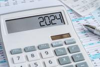 A calculator with &quot;2024&quot; in its display sits on top of some financial charts.